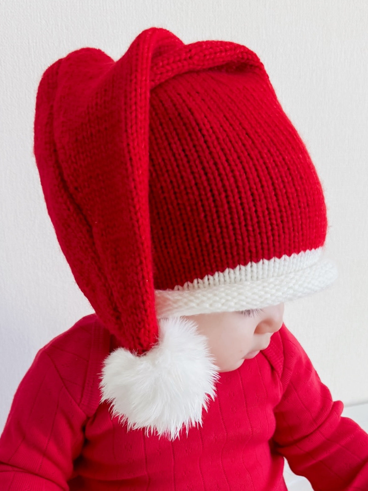 Child wearing a red festive Santa hat with a white pom-pom, dressed in a matching red sweater.