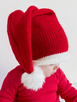 Child wearing a red festive Santa hat with a white pom-pom, dressed in a matching red sweater.