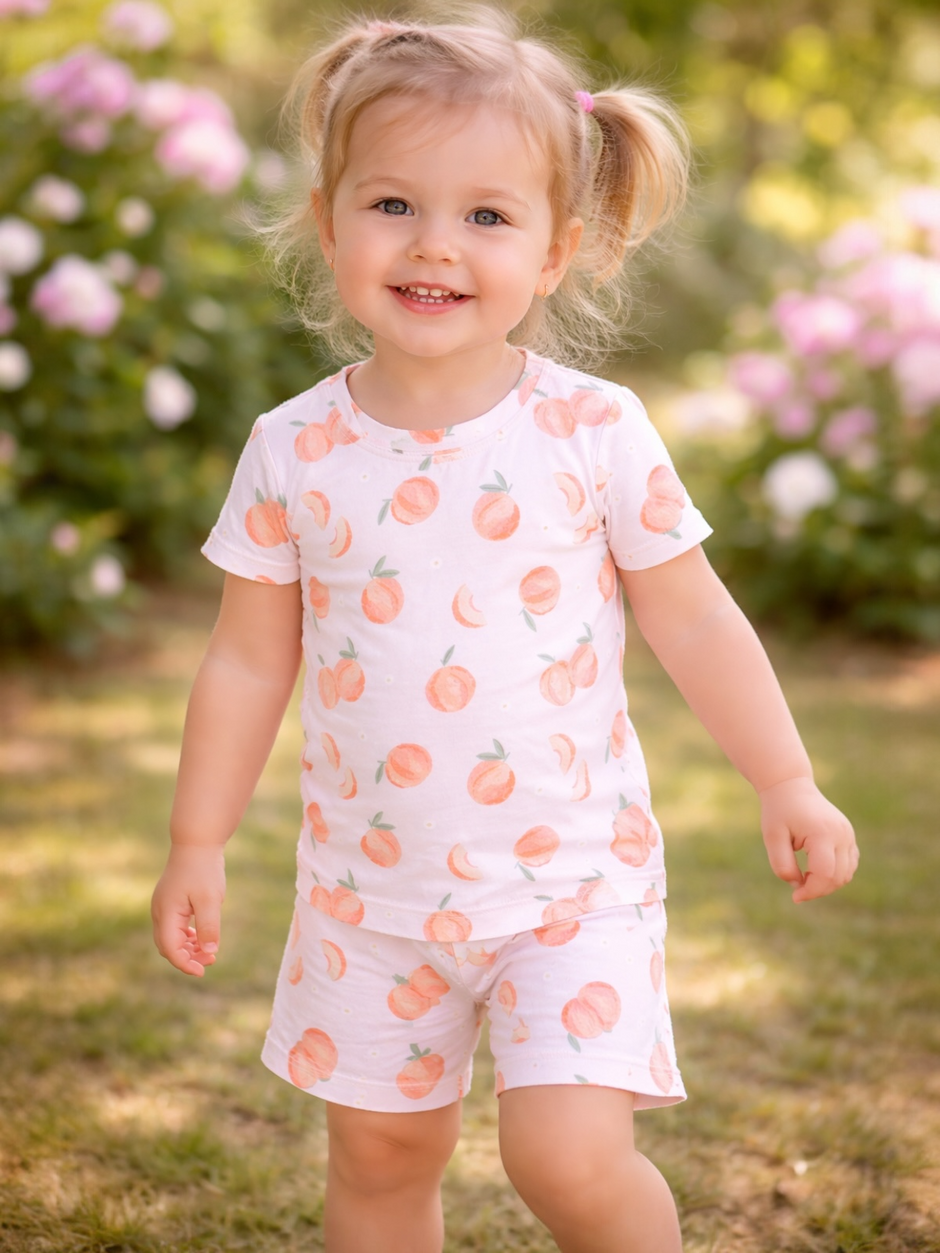 Smiling toddler in peach-patterned outfit, walking happily in garden with blooming flowers in the background.