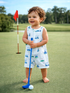 Smiling toddler in a golf-themed outfit holds a blue putter on a lush green golf course.