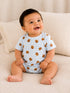 Smiling baby in a blue checked onesie with bear print, seated on a cozy beige blanket.