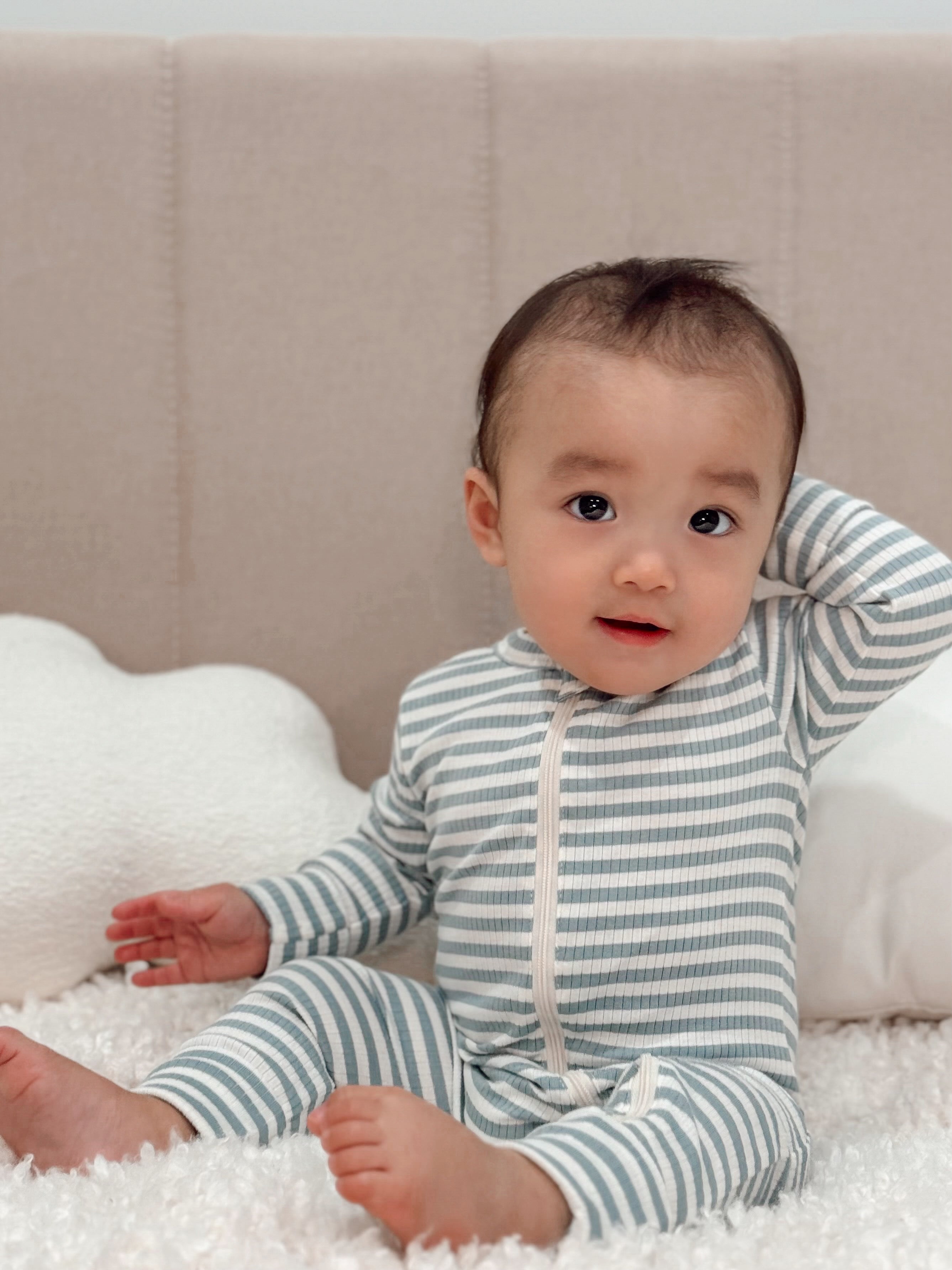 Baby sitting on a plush blanket, wearing a striped onesie, smiling and playing with a cloud-shaped pillow.