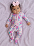 Smiling baby in floral pajamas with a pink bow, lying on a soft purple blanket.