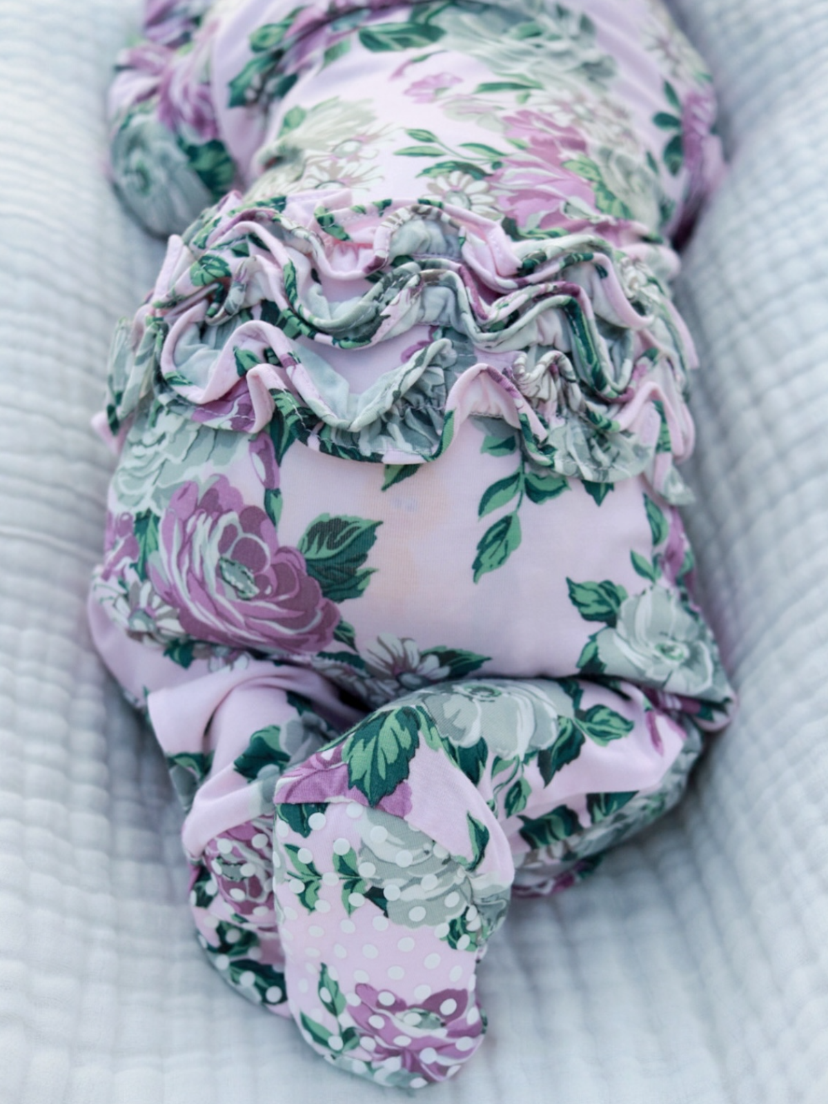Floral fabric swaddled around a baby, resting on a soft, textured white blanket.