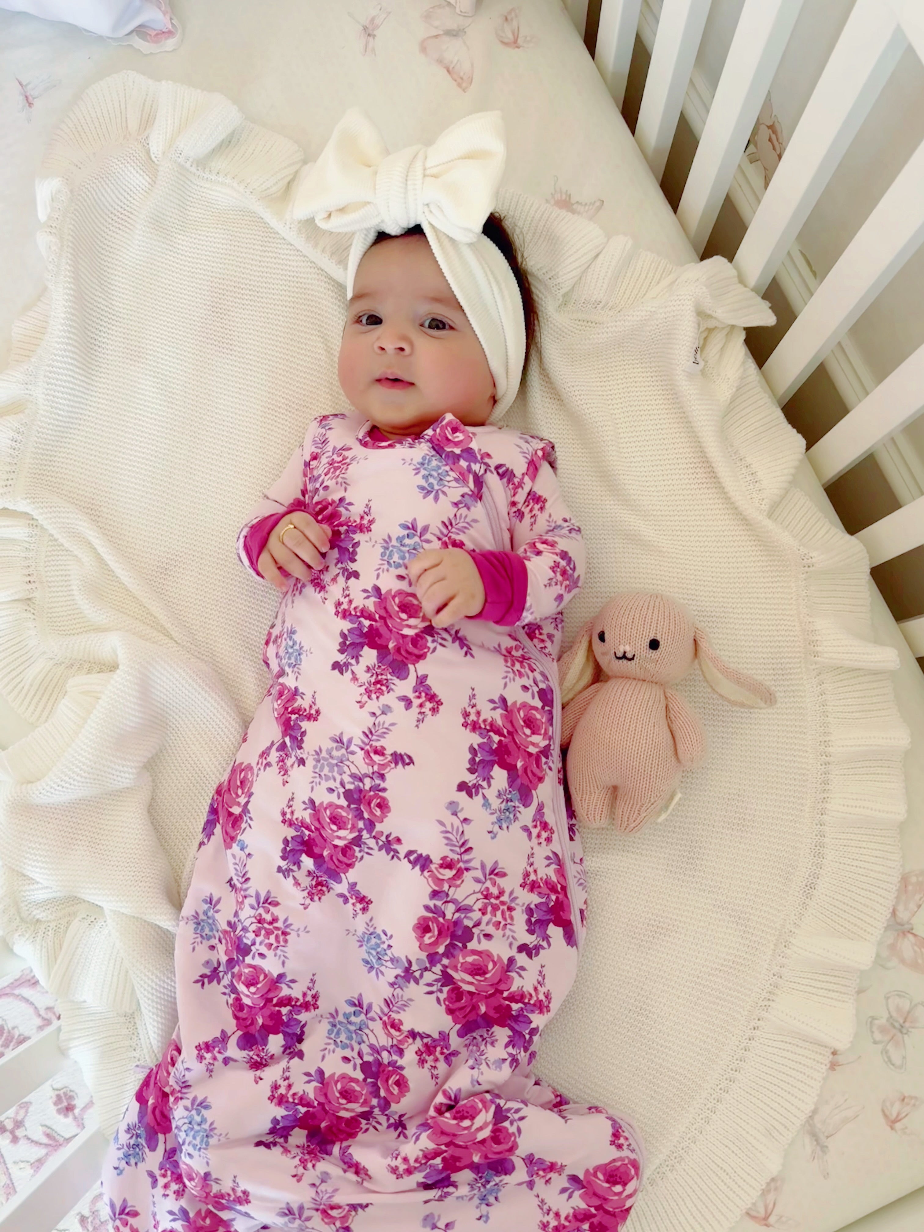 Infant in floral swaddle on a blanket, wearing a headband, with a plush bunny stuffed toy nearby.