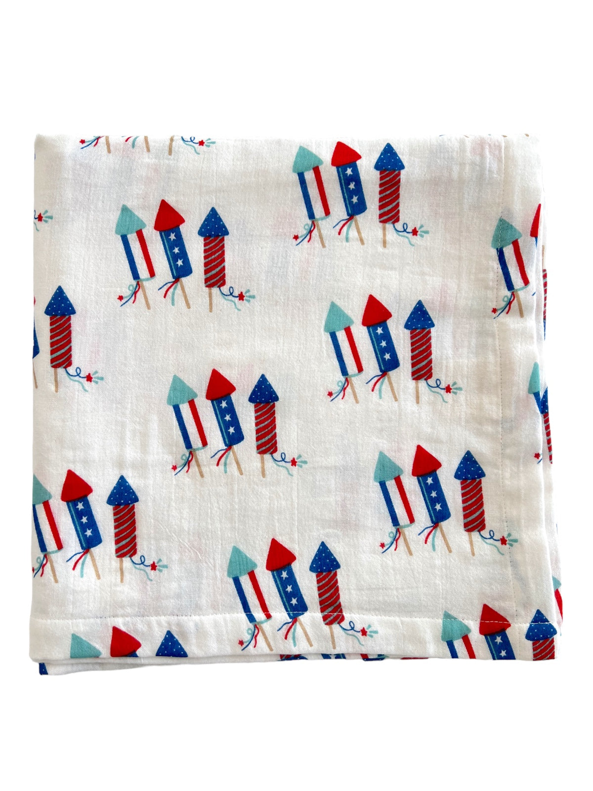 White fabric with a playful pattern of colorful rockets in red, blue, and green, perfect for festive occasions.