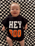 Smiling baby in a black sweater with "HEY BOO" on a checkered blanket.