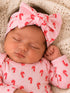Sleeping baby girl wearing a candy-cane patterned outfit and a large pink bow on a knit blanket.