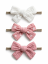 Three hair accessories: a white bow, a pink bow with polka dots, and a solid pink bow on elastic bands.