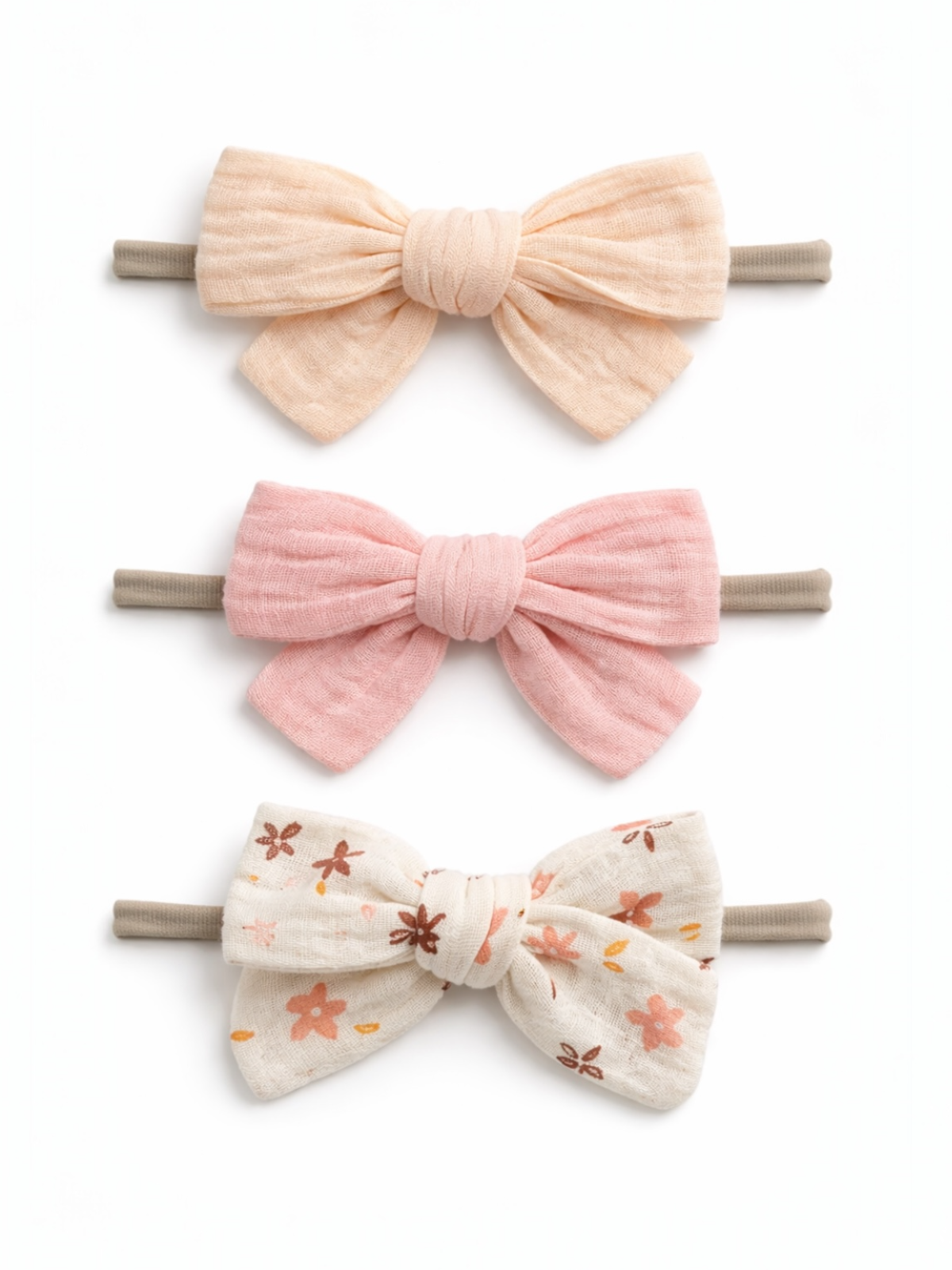 Three hair bows in soft colors: peach, pink, and floral patterns on a white background, attached to elastic bands.