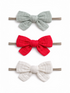 Three fabric hair bows in gray, red, and white on elastic bands, arranged vertically against a white background.
