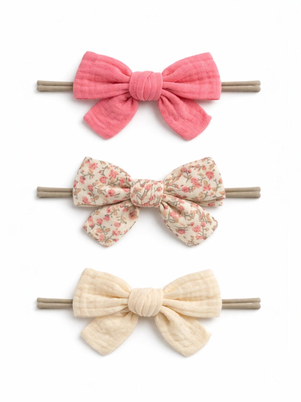 Three hair bows: pink, floral print, and cream, all attached to elastic bands on a white background.