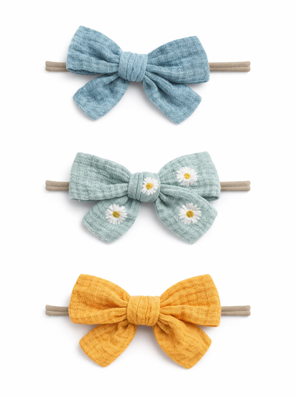 Three colorful fabric hair bows: blue, green with daisies, and yellow, tied on elastic bands.