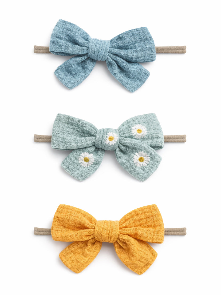 Three colorful fabric hair bows: blue, green with daisies, and yellow, tied on elastic bands.