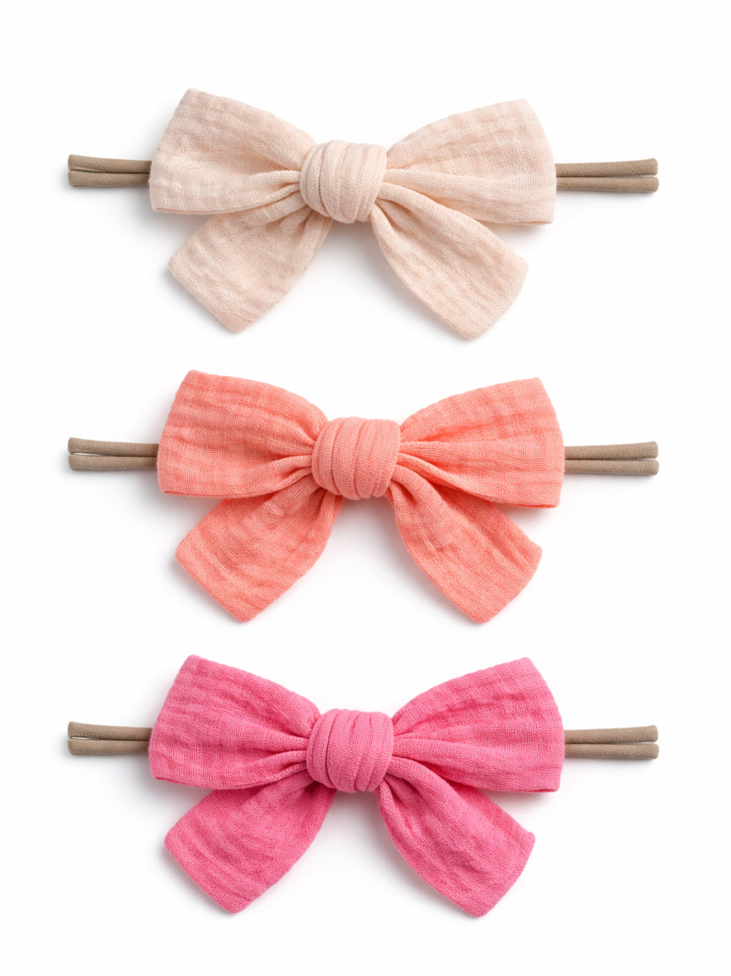 Three fabric hair bows in soft colors: cream, coral, and pink, attached to elastic bands.