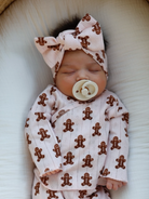 Newborn baby sleeps in pink gingerbread-patterned outfit with a matching headband and pacifier.