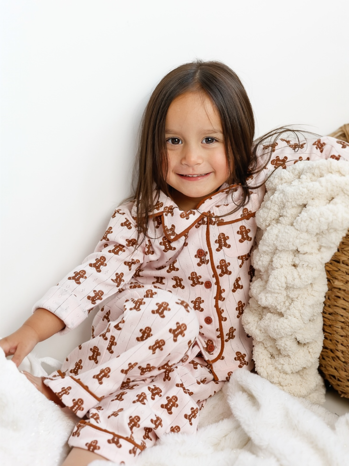 Smiling girl in gingerbread-printed pajamas sitting on cozy blankets.