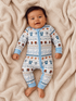 Smiling baby in a sporty onesie on a cozy blanket, surrounded by playful football-themed patterns.
