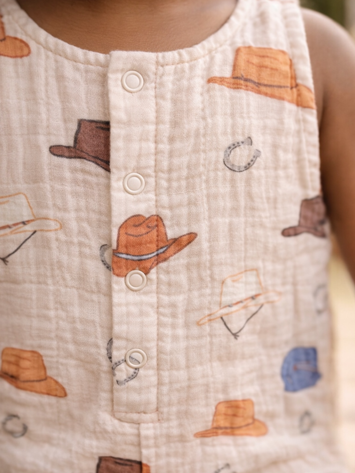 Close-up of a child's shirt featuring a pattern of colorful hats and buttons on a soft, textured fabric.