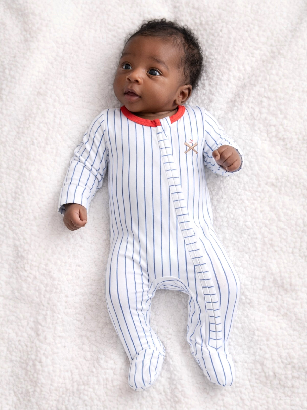 Baby in a striped onesie, looking up while lying on a soft blanket.