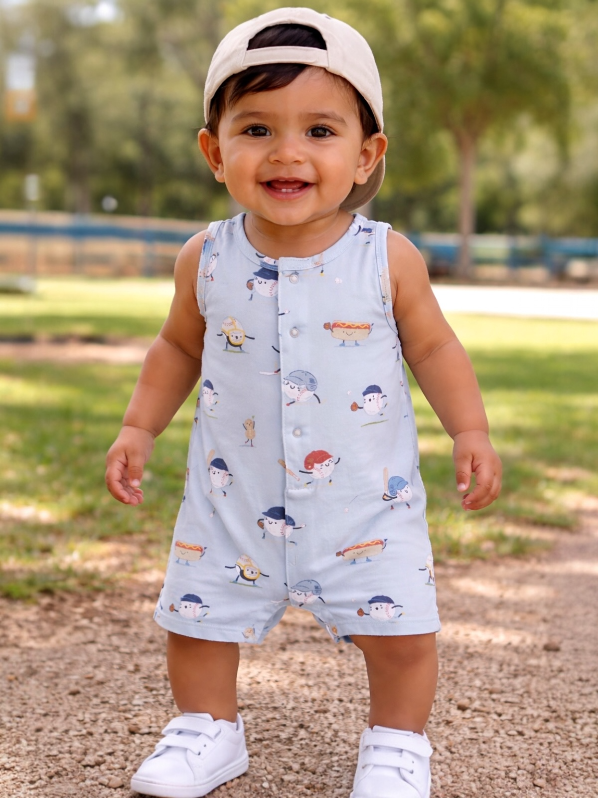 Smiling toddler in a playful outfit with cartoon food designs, standing in a sunny park setting.