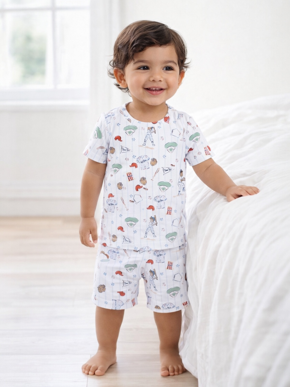 Smiling toddler in playful pajamas, standing by a bed in a bright, airy room.