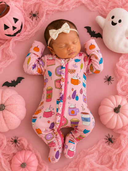 Sleeping baby in a pink patterned onesie surrounded by pumpkins, a ghost, and Halloween decor.