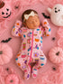 Sleeping baby in a pink patterned onesie surrounded by pumpkins, a ghost, and Halloween decor.