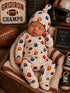 Newborn sleeping in a football-themed outfit, surrounded by sports memorabilia and cozy blankets.