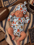 Baby boy sleeping on a blanket, wearing a colorful sports-themed onesie and matching hat, with a football nearby.