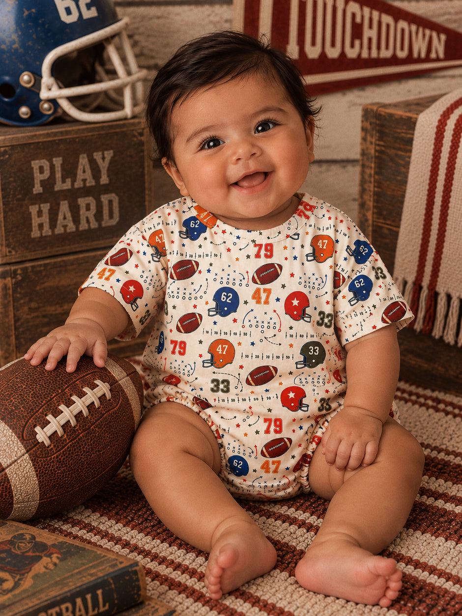 Smiling baby in a football-patterned onesie, sitting with a football and sports-themed background.