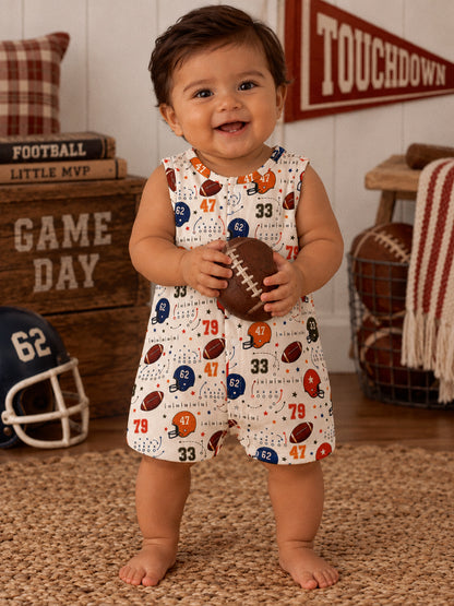 Smiling baby in a football-patterned romper, holding a football in a cozy, sports-themed room.