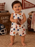 Smiling baby in a football-patterned romper, holding a football in a cozy, sports-themed room.