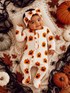 Smiling baby in a pumpkin-patterned onesie with a matching headband, surrounded by fall decorations.