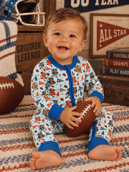 Smiling baby in pajamas holding a football, surrounded by sports-themed decor and a cozy rug.