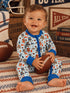 Smiling baby in pajamas holding a football, surrounded by sports-themed decor and a cozy rug.