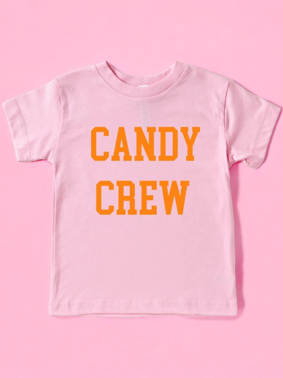 Pink t-shirt with orange text that reads "CANDY CREW." Background is solid pink.