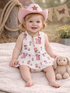 Smiling toddler in a pink cowgirl hat sitting on a blanket with a stuffed bunny toy. Playful and cheerful atmosphere.