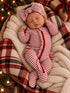 Infant asleep in a cozy, striped outfit with a bow headband, nestled in a soft blanket surrounded by festive decor.