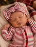 Sleeping baby in red and white striped outfit with a large bow, resting on textured blanket. Cozy holiday setting.