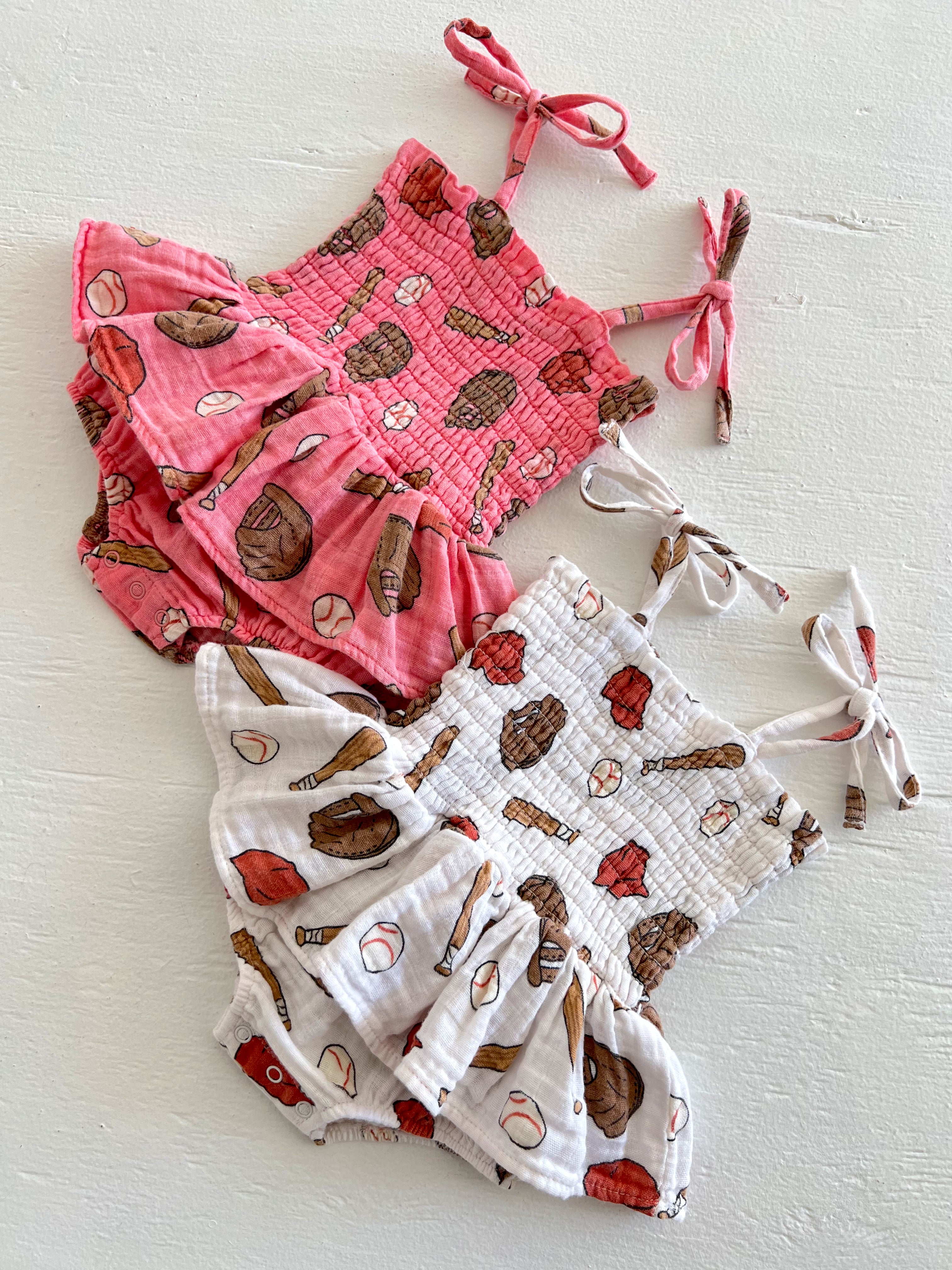 Two children's rompers in pink and white with playful ice cream and baseball prints, featuring ruffled edges and tie straps.