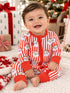 Toddler in festive striped pajamas with Santa faces, smiling on a soft rug surrounded by holiday gifts.