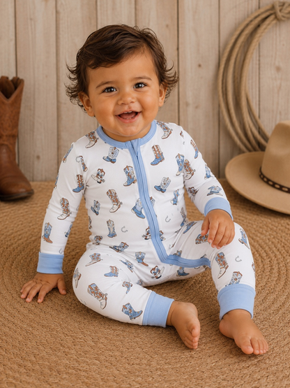 Smiling toddler in cowboy-themed pajamas sits on a woven rug, with a cowboy boot and hat in the background.
