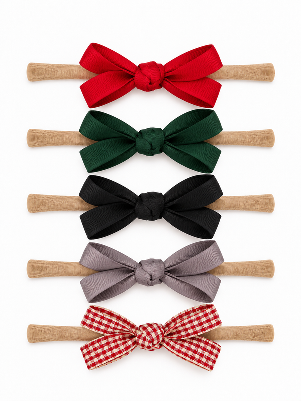 Five hair accessories with colorful bows in red, green, black, gray, and a red checkered pattern on beige bands.