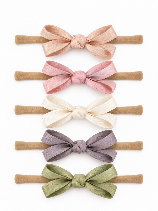 Five hair ties with bows in pink, cream, lavender, and green on a white background. Perfect for cute hairstyles.