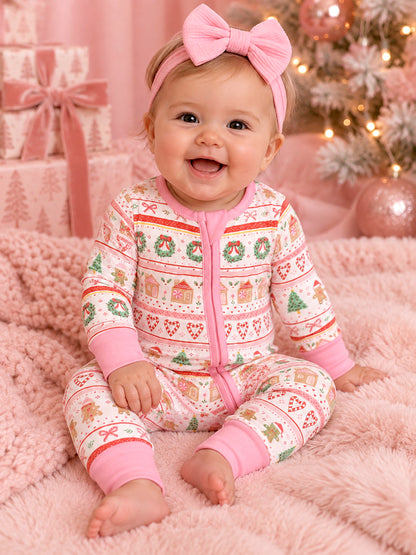 Smiling baby in a festive onesie with holiday patterns, sitting on pink fur blanket with Christmas tree and gifts.