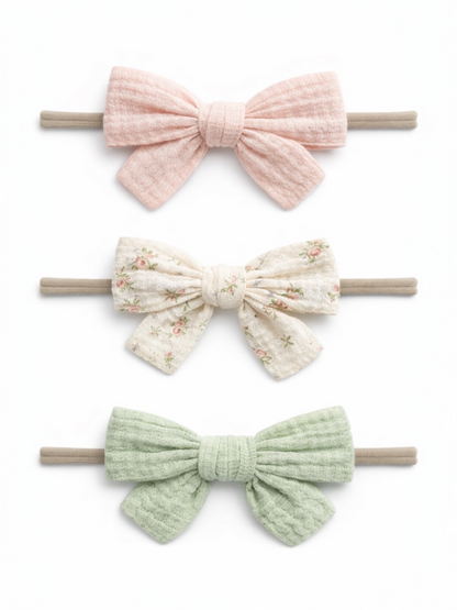 Three hair bows in pink, floral, and green colors on elastic bands against a white background.