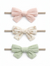 Three hair bows in pink, floral, and green colors on elastic bands against a white background.