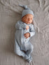 Newborn baby in a light blue outfit and hat, peacefully sleeping on a soft, neutral-colored blanket.