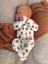 Sleeping baby in a gingerbread-patterned onesie, peacefully cradled on a soft blanket.